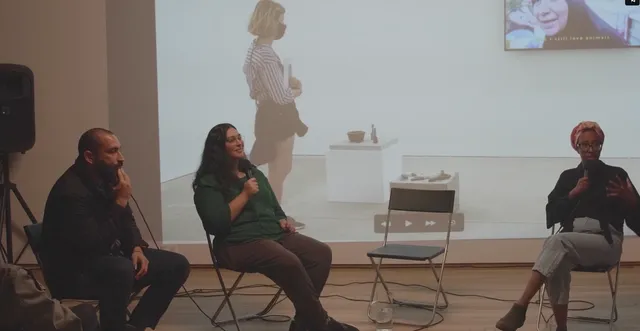 Three people in conversation on the chairs with microphones in front of a video projection on the wall.