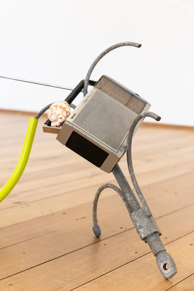 A detail shot of a radio on metal hooks with a shell resting on top.