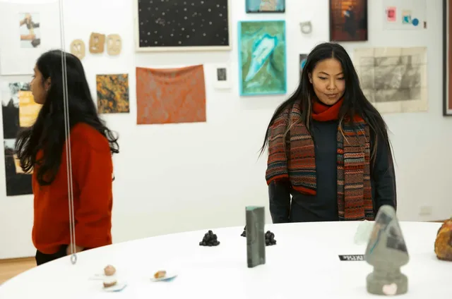 Two figure are admiring a large round platform covered in small sculptural objects during the West Space fundraiser 2024