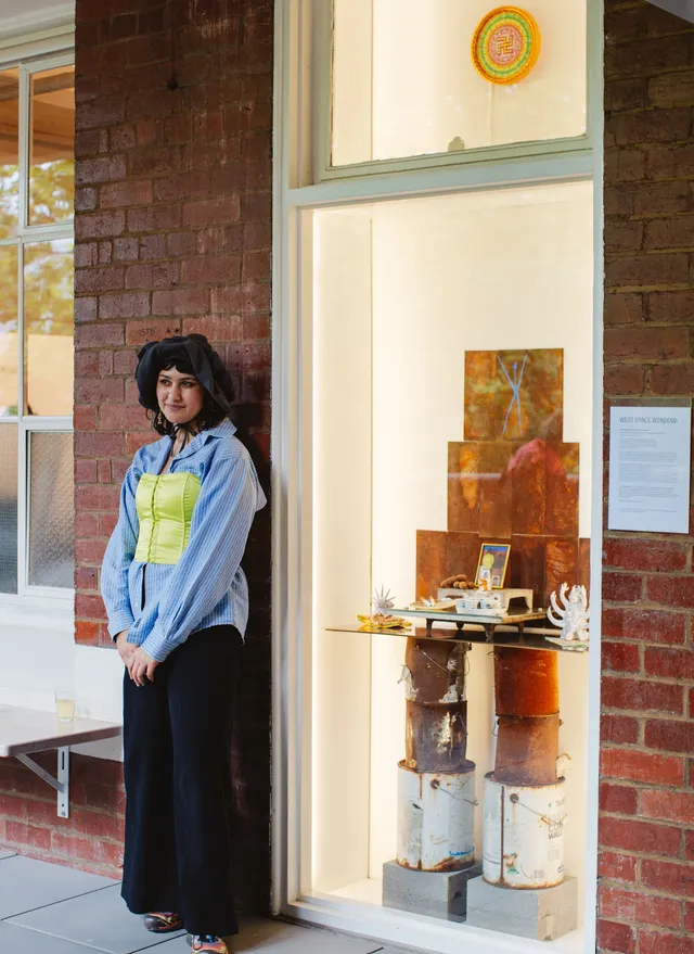 A person stands next to a brick wall and a display window with various objects inside.