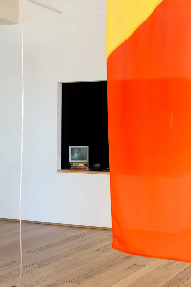 Installation view of "Big Pharmakon". A red and yellow sheet covers the right side of the image and a small blank analog television is visible in the background sitting on a countertop.