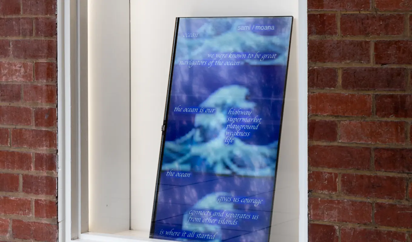 A screen leaning behind a shallow window display, on its side. The screen depicts a deep blue landscape with the silhouette of a tree in the bottom corner. There are shades of clowd.