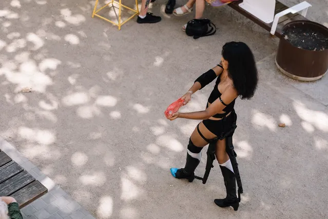 Ari walking on gravel wearing all black and holding an orange fish like she is holding a gun.