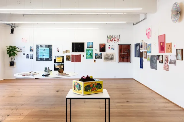 A wide angle photograph of the installation of the west space fundraiser. Many, many artworks are hung on the walls in a salon hang style with 2 separate shelves and plinths installed in the space.