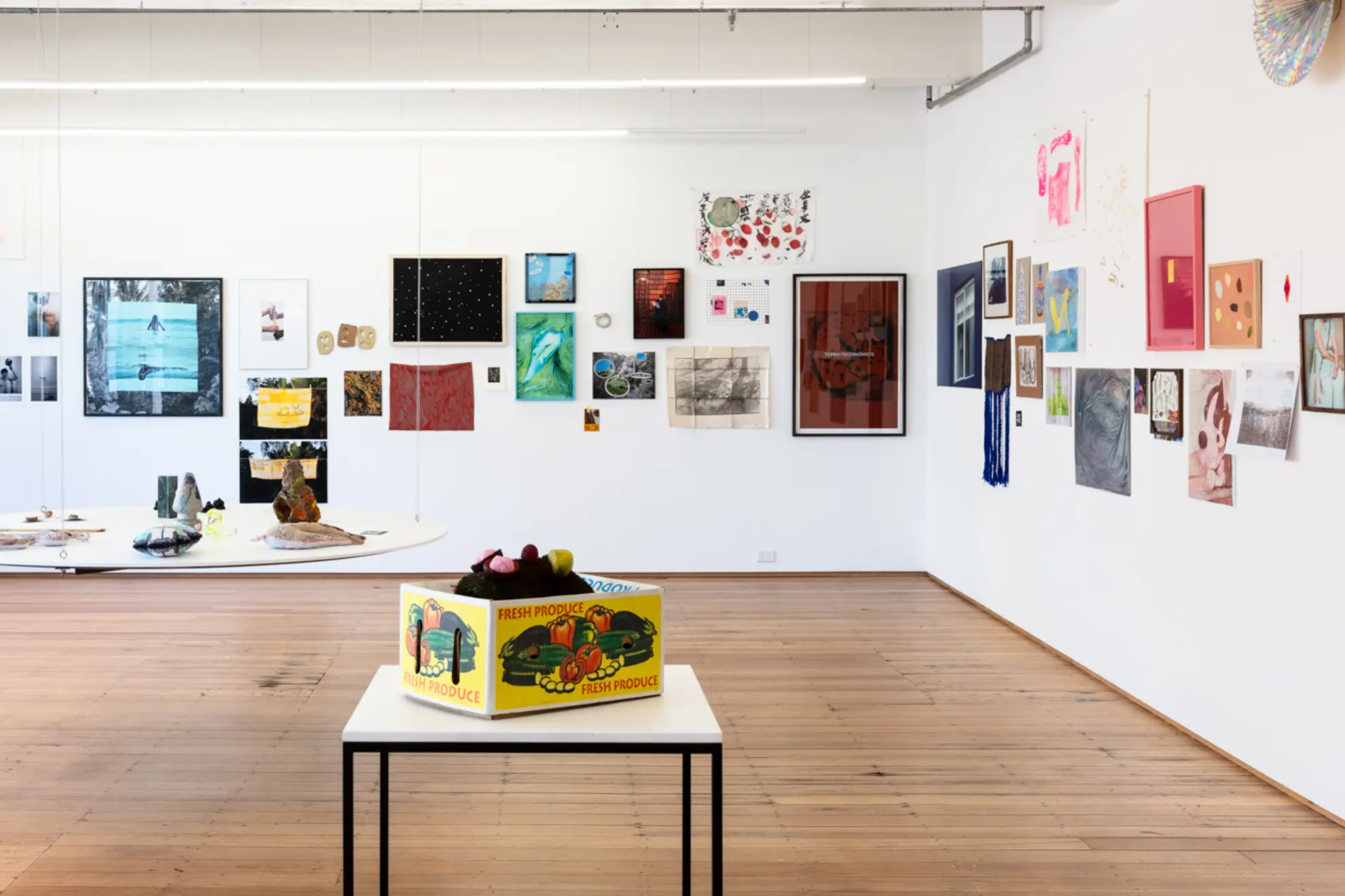 A wide angle photograph of the installation of the west space fundraiser. Many, many artworks are hung on the walls in a salon hang style with 2 separate shelves and plinths installed in the space.