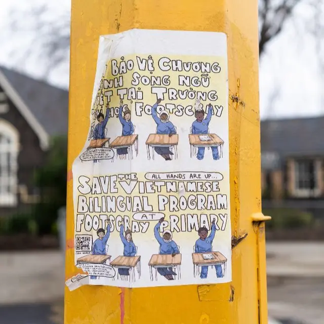 A paper poster in English and Vietnamese to save the Vietnamese bilingual program at Footscray Primary School, stuck to a yellow pole.