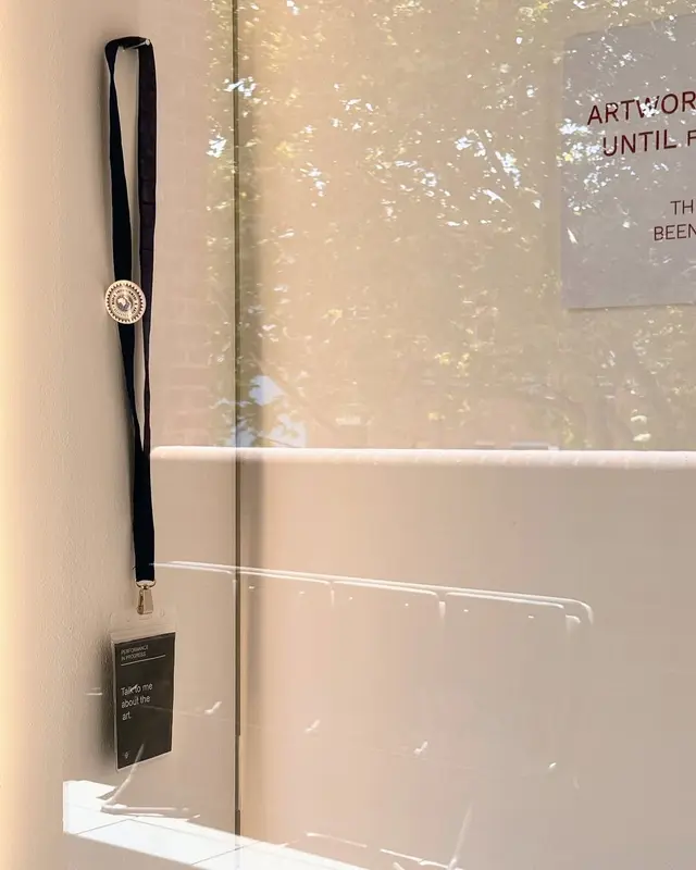 Behind the window, a black lanyard hangs from a nail on the left, while part of an artwork is visible on the right.