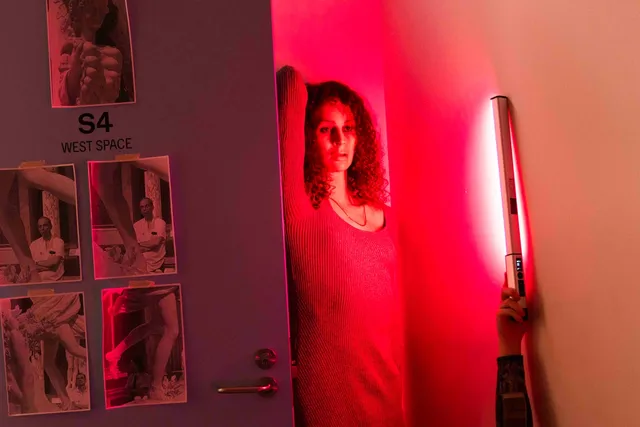 A figure bathed in Pink and Red light stands behind a blue door that has black and white pictures of marble statues taped to it. On the door it says "S4 WEST SPACE"