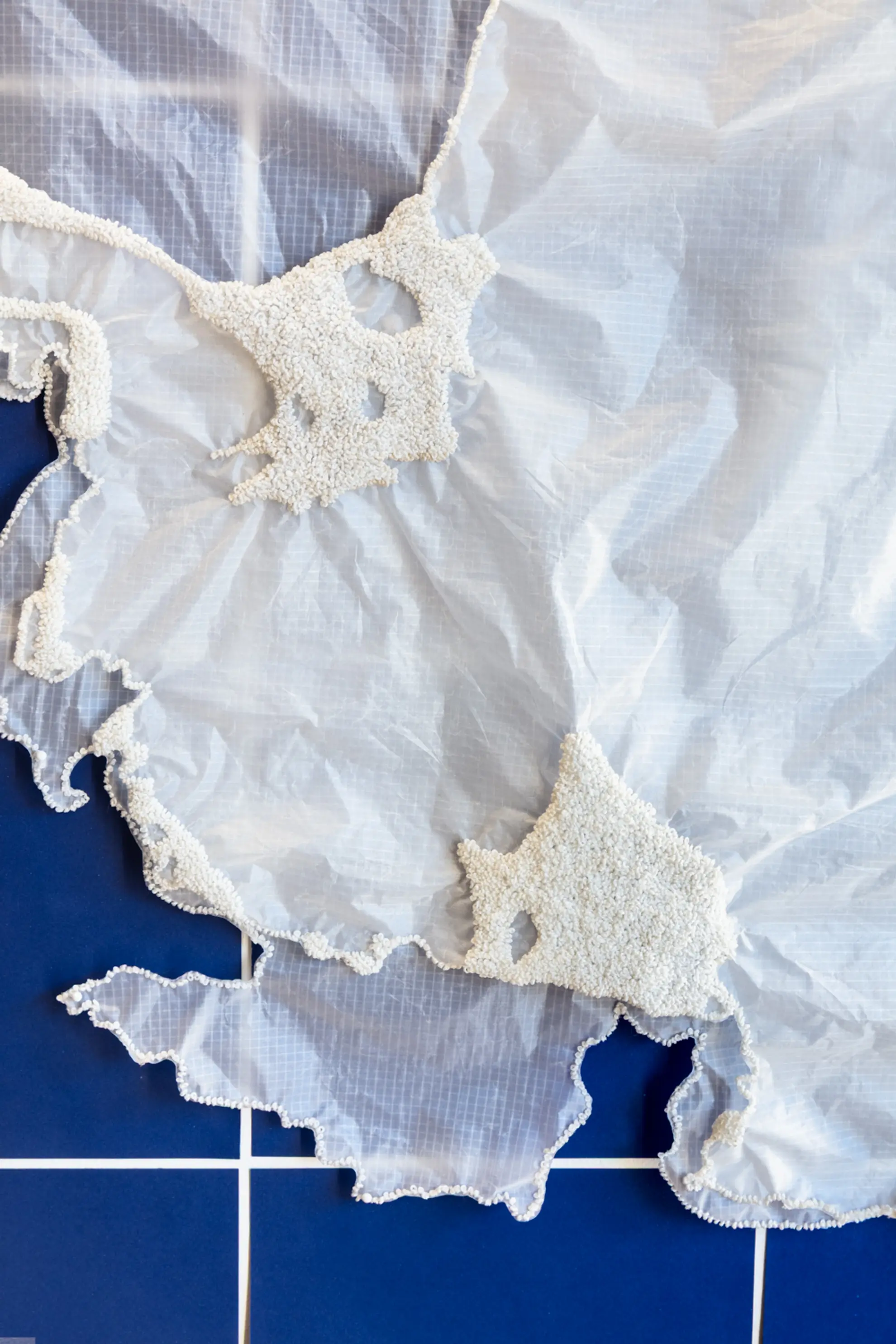 A detail shot of layered sheer, crinkled fabric. There are hundreds of tiny white beads fixed in clusters to the fabric.