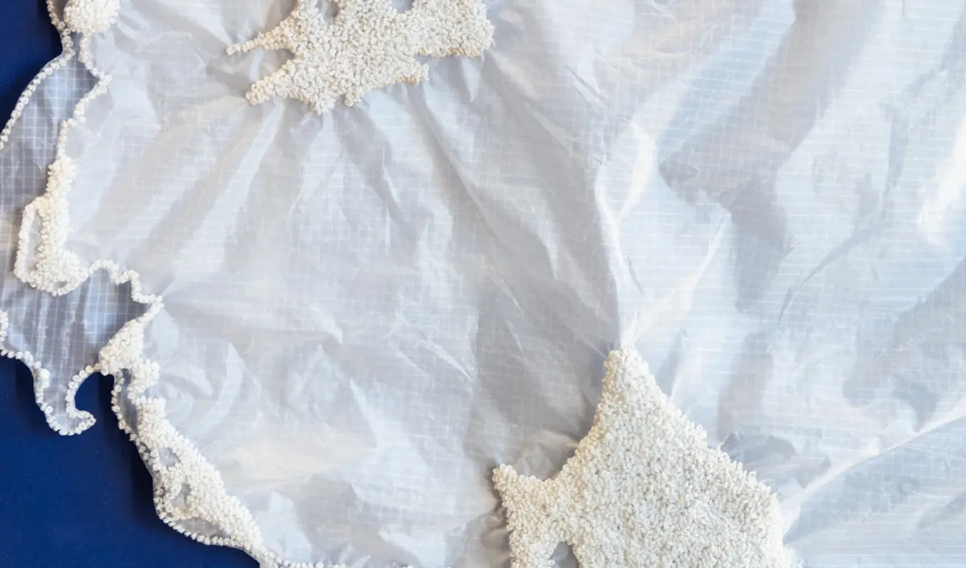 A detail shot of layered sheer, crinkled fabric. There are hundreds of tiny white beads fixed in clusters to the fabric.
