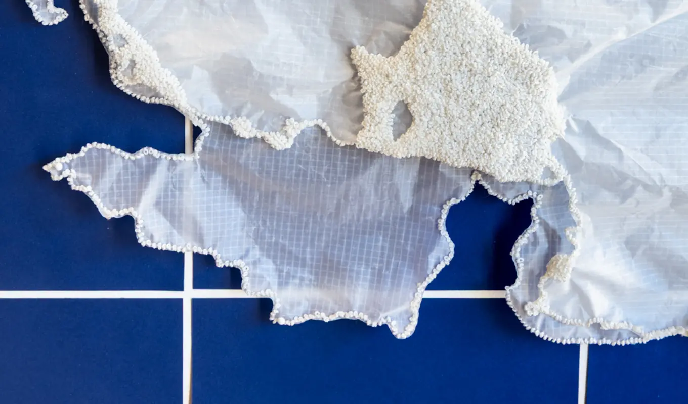 A detail shot of layered sheer, crinkled fabric. There are hundreds of tiny white beads fixed in clusters to the fabric.