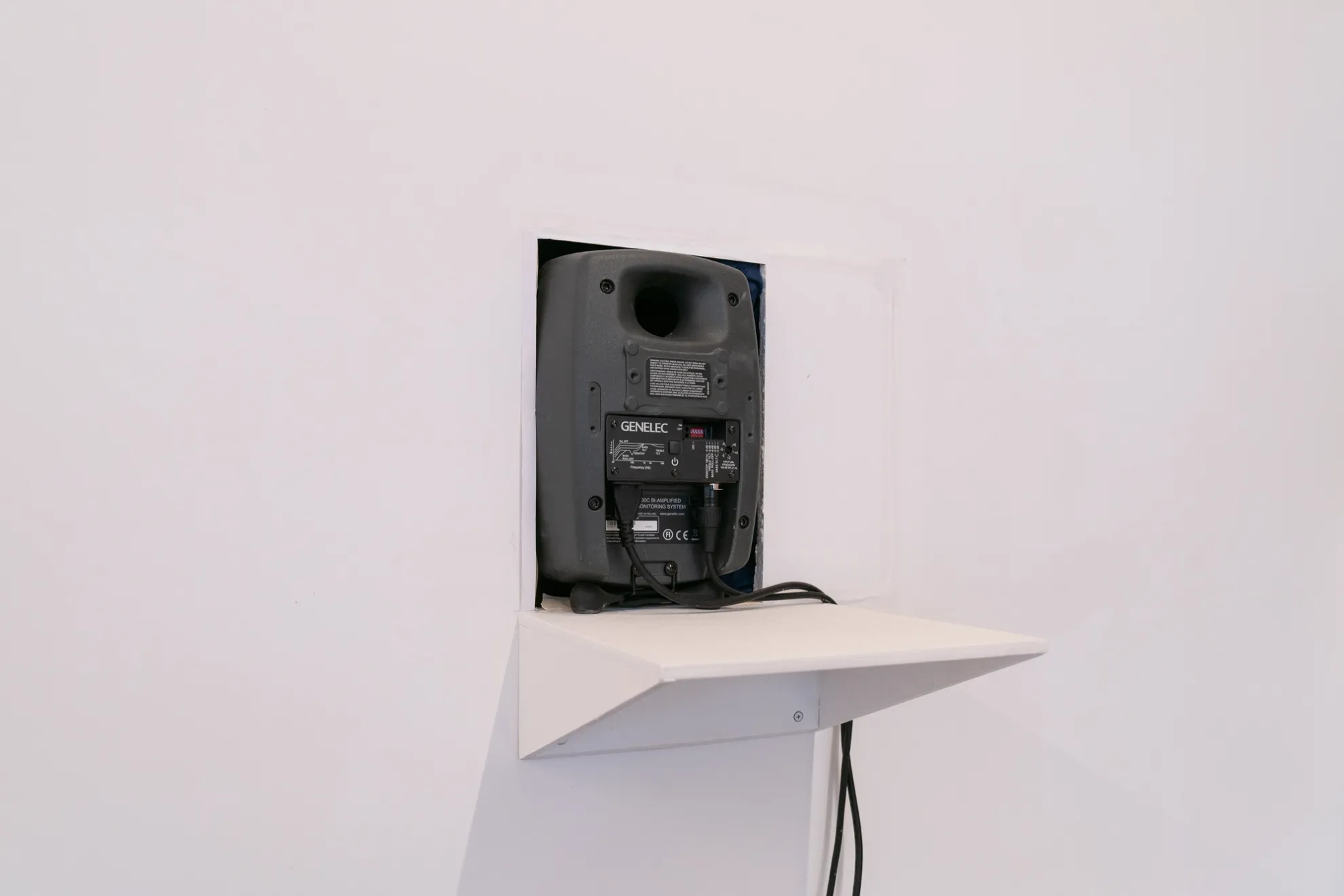 The back of an amp enclosed in a white wall within a built-in shelf. In-front and below the the amp is a large, portruding triangular lip.