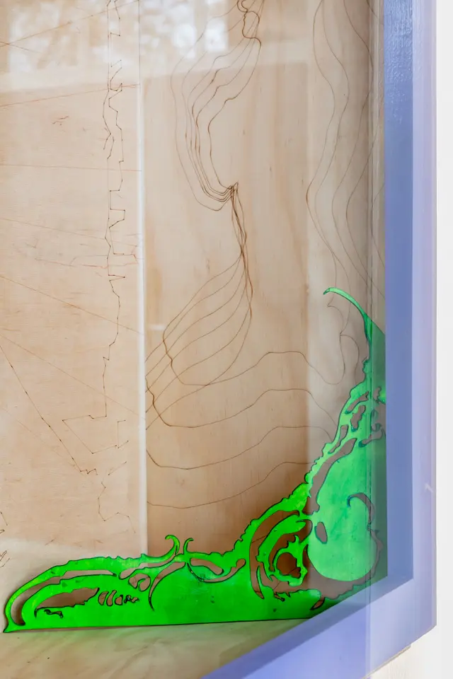 Close-up of an intricately laser-cut wood piece design painted in a bright green sitting in the corner of a larger sheet of wood.
