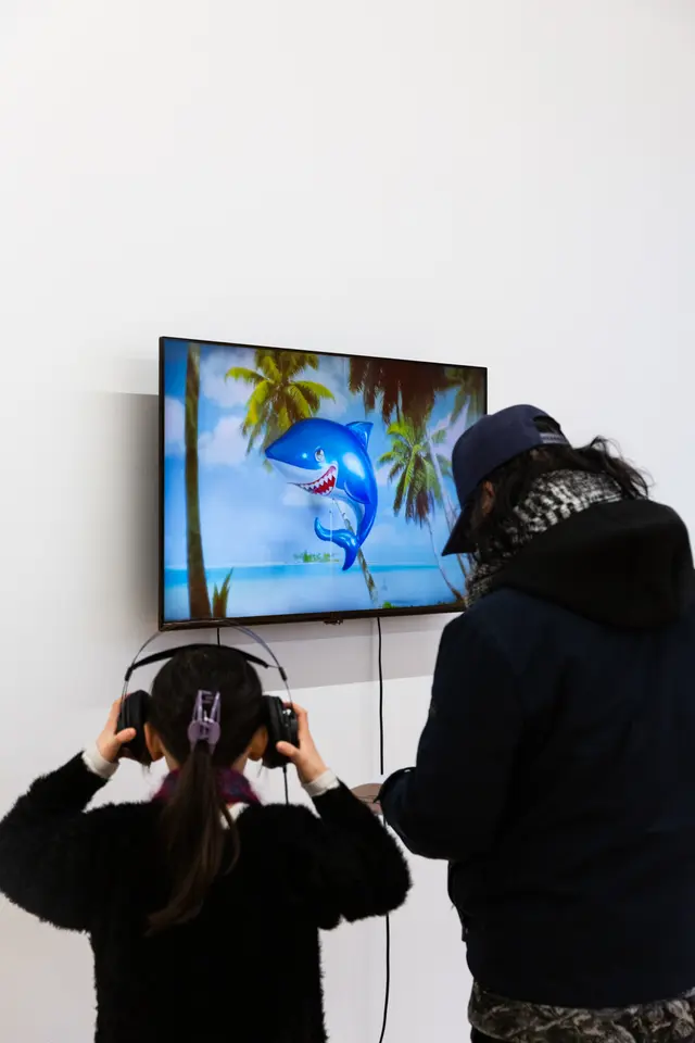 2 figures stand in front of television screen depicting a large inflatable shark balloon