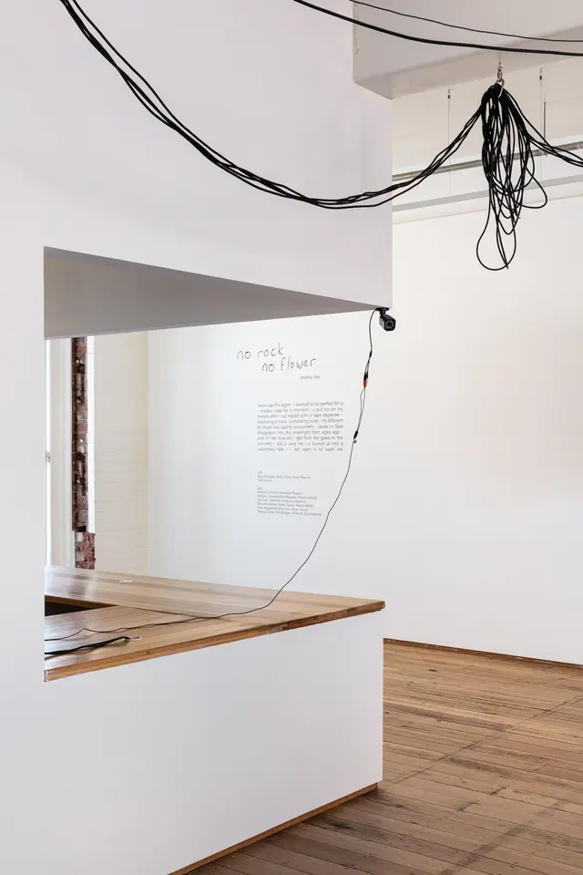A CCTV camera and wires are attached to the ceiling. Wall text of the exhibition is in the back.
