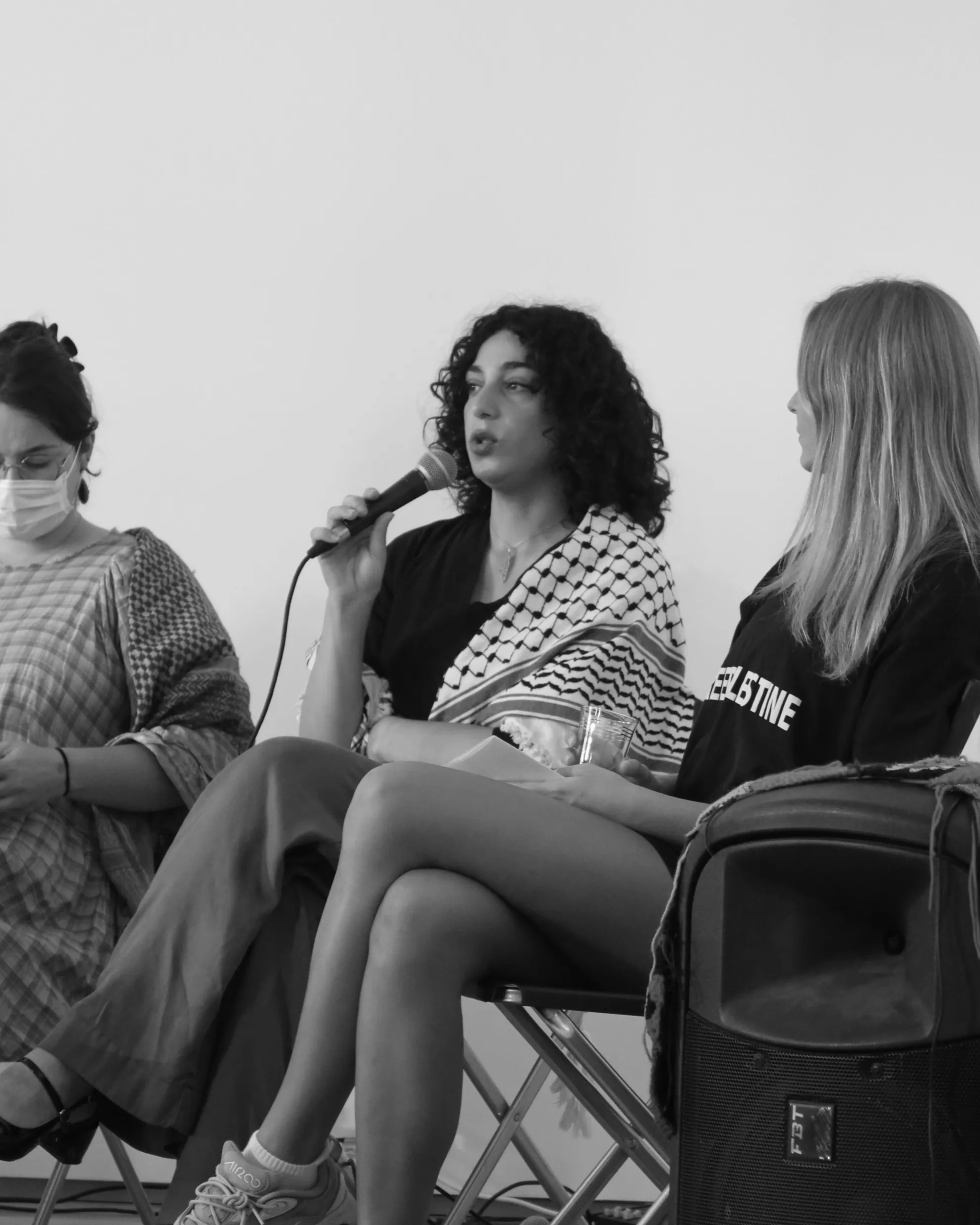 A black-and-white image of three people, the person in the middle is speaking with a microphone.