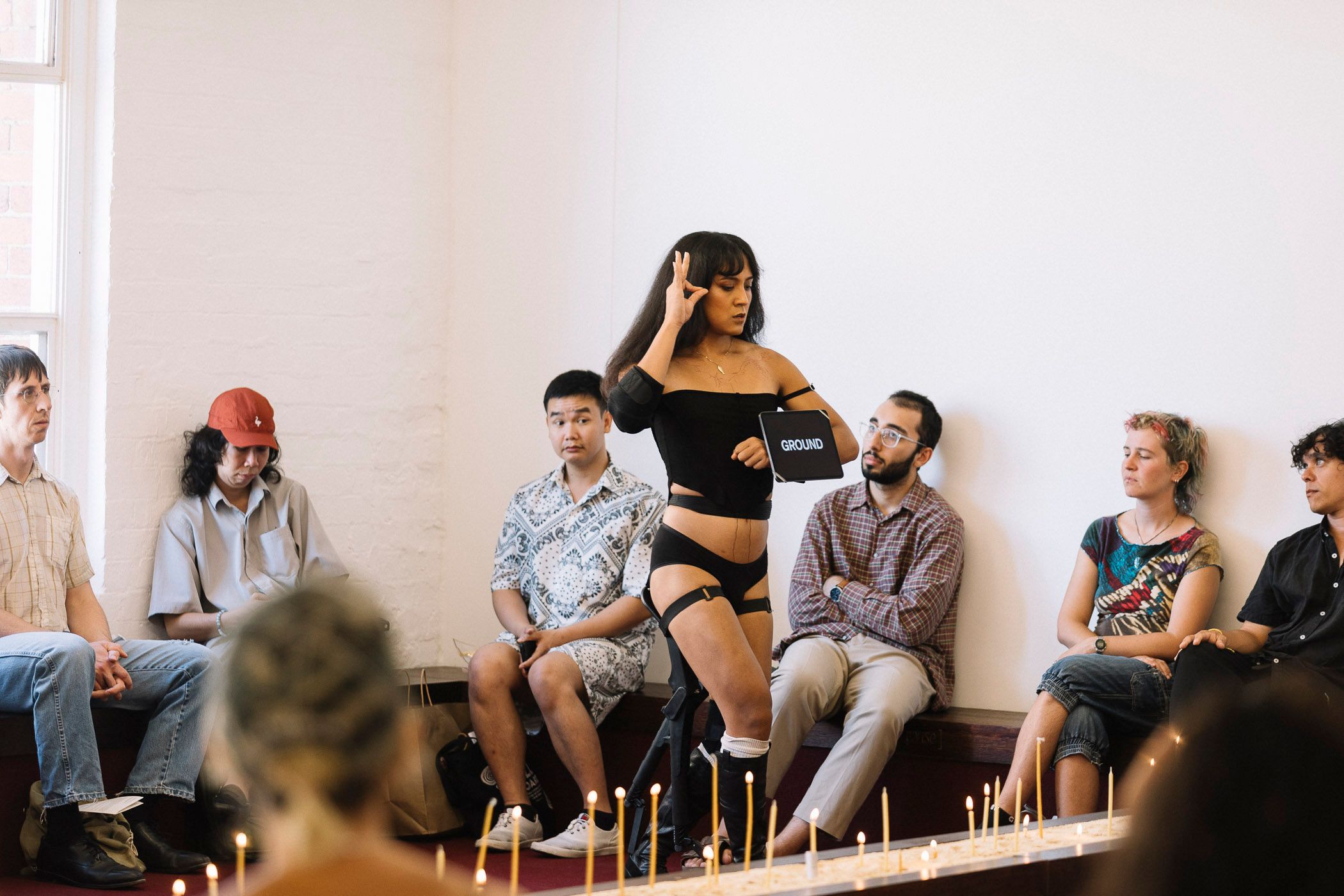 Ari performing among a crowd of watching audience members. She is displaying an ipad with text and a hand gesture next to her face.