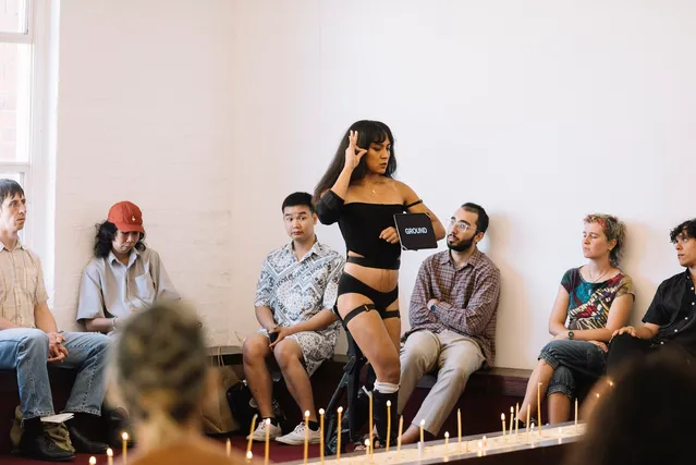 Ari performing among a crowd of watching audience members. She is displaying an ipad with text and a hand gesture next to her face.