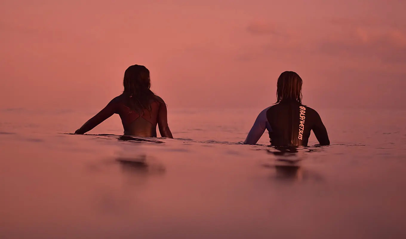 The back of two people on their surfboards in the ocean.