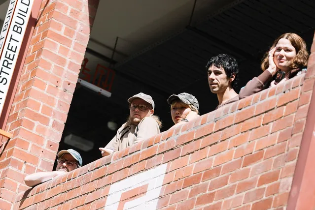 A group of people with their heads peering over a brick balcony.