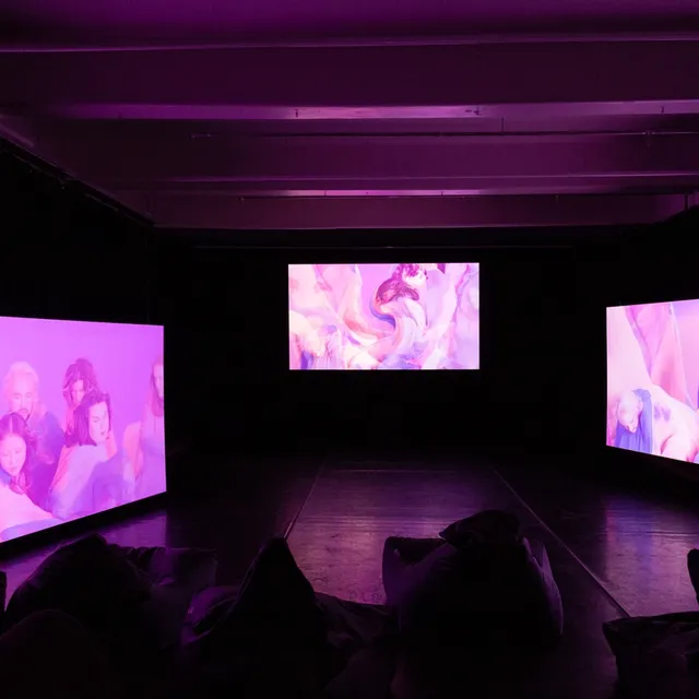 People watching videos displaying on three screens in the dark.