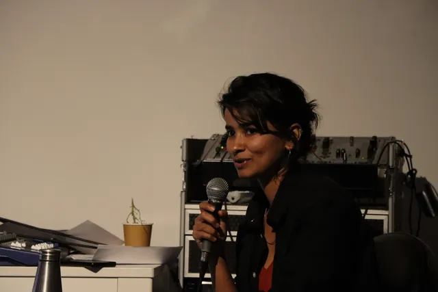 A photograph of Aasma Tulika speaking into a microphone.