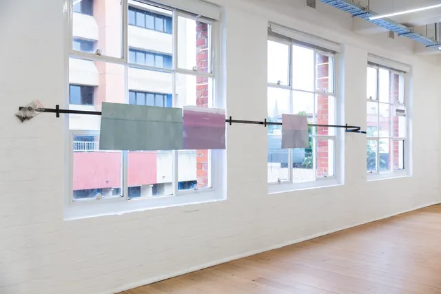 A view out of West Space gallery windows featuring the work of Rosie Isaac. A steel bar stretches across several windows with objects attached to it with magnets.