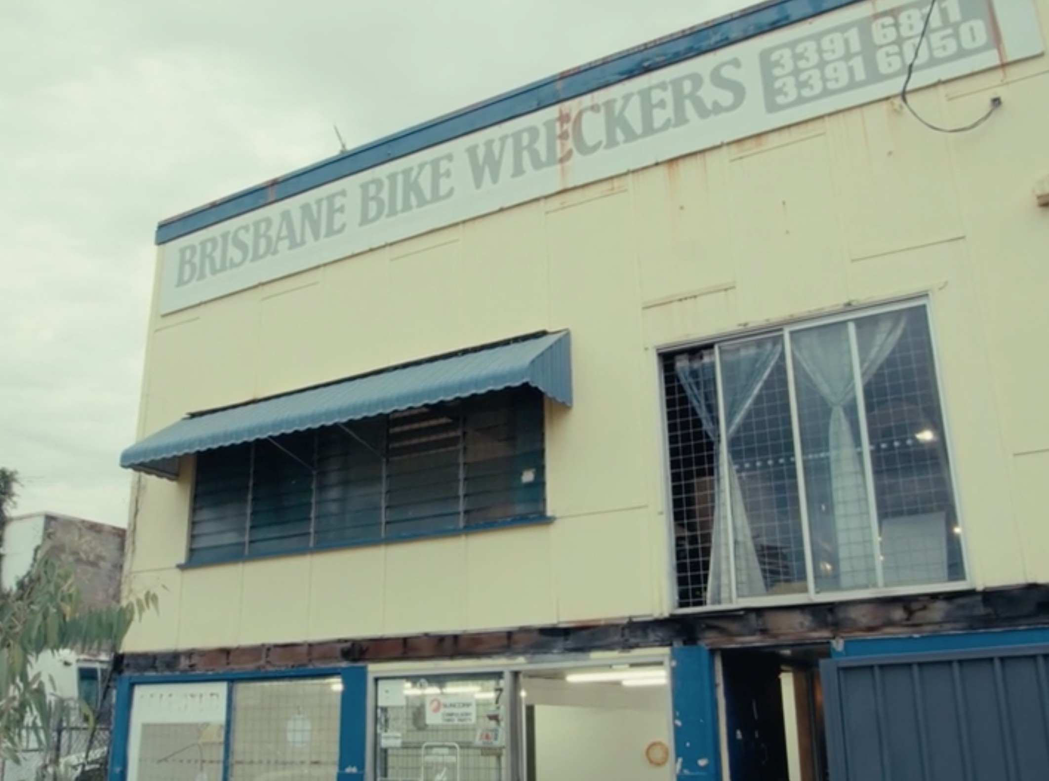 A cream and blue building with windows, doors, and the sign "BRISBANE BIKE WRECKERS".