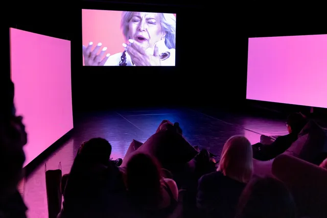 People watching videos displaying on three screens in the dark.