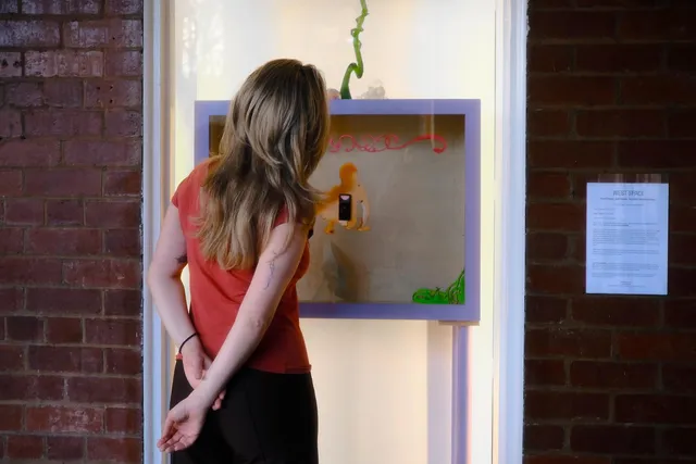 A figure with long blonde hair and wearing a red shirt viewing Yanti Pengs 'Self-made: Invisible Architectures' with their hands behind their back.