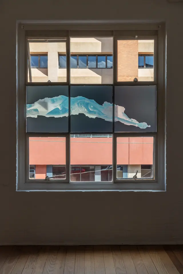A negative photo of a woman lying down is displayed on the windows of a dim room.