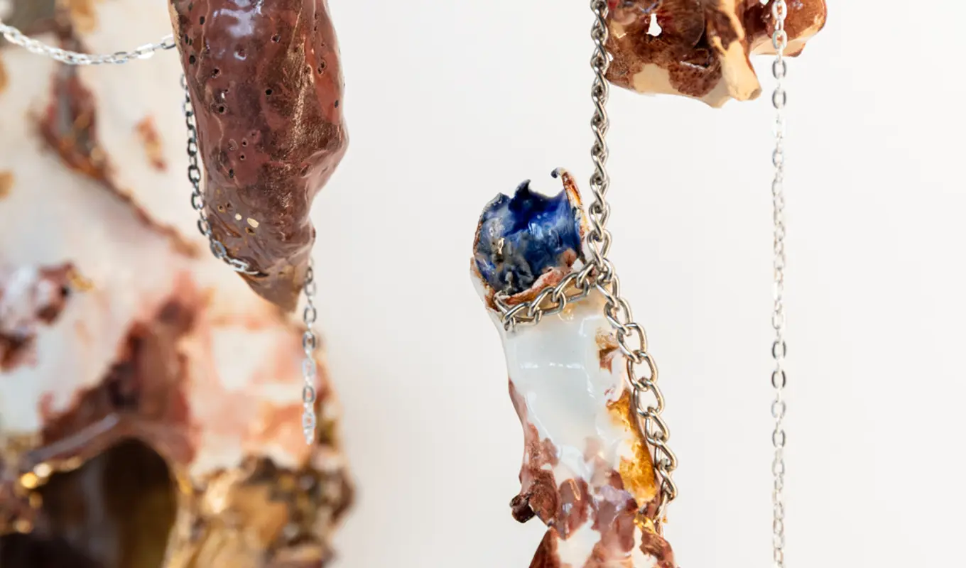 Three marbled brown, blue and white porcelain sculptures hang from silver chains of varying link sizes.