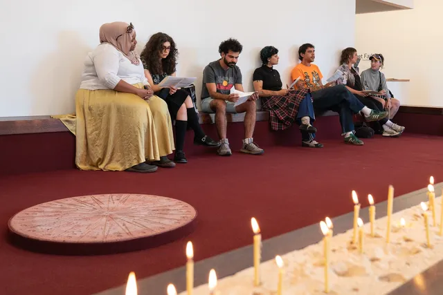 A group of audience members sitting along a wooden bench as part of participating in Tina Stefanou's 'Motet Fail'.