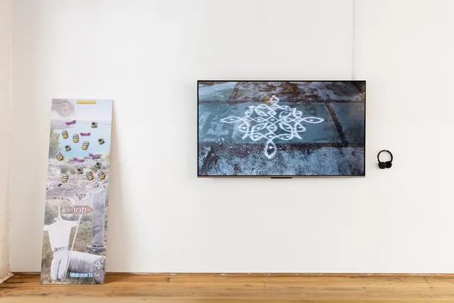 A TV at the right displays white patterns drawn on tiles; a printed board with magnets is on the left.