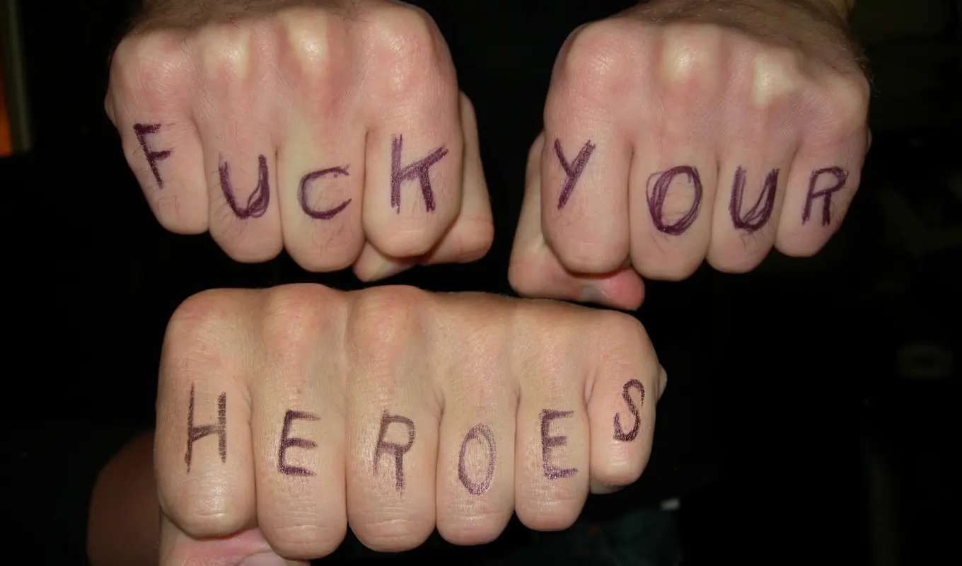 Three peoples fists with the words 'Fuck Your Heroes' scribbled onto each finger with pen.