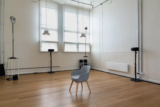A chair in the middle of the room, surrounded by lights and several speakers.
