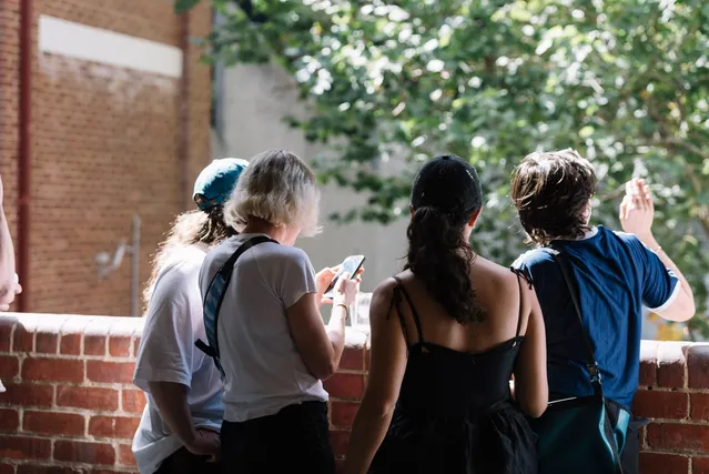 A group of four people with their backs to the camera looking out over a brick balcony.
