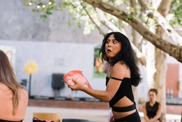 Ari with a surprised and shocked look on her face holding an orange fish like a gun.
