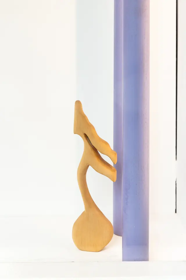 Close-up of a wooden sculpture resembling a music note leaning up against two purple poles.