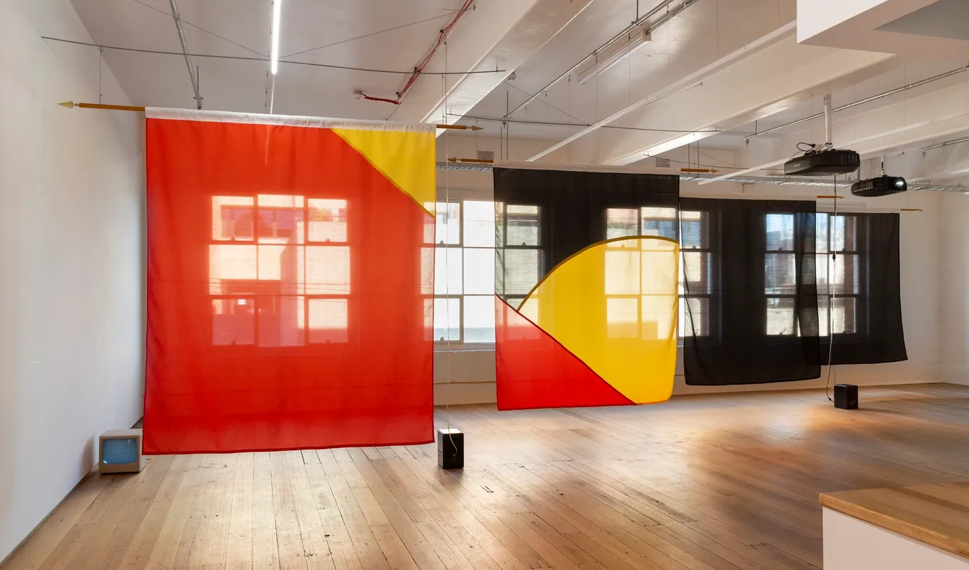 The indigenous flag in large transparent, fabricated fragments, in a group of 4 large segments. The transparent sheets are reminiscent of divides of the indigenous flag and colours, suspended from the ceiling and pertruding into the space.