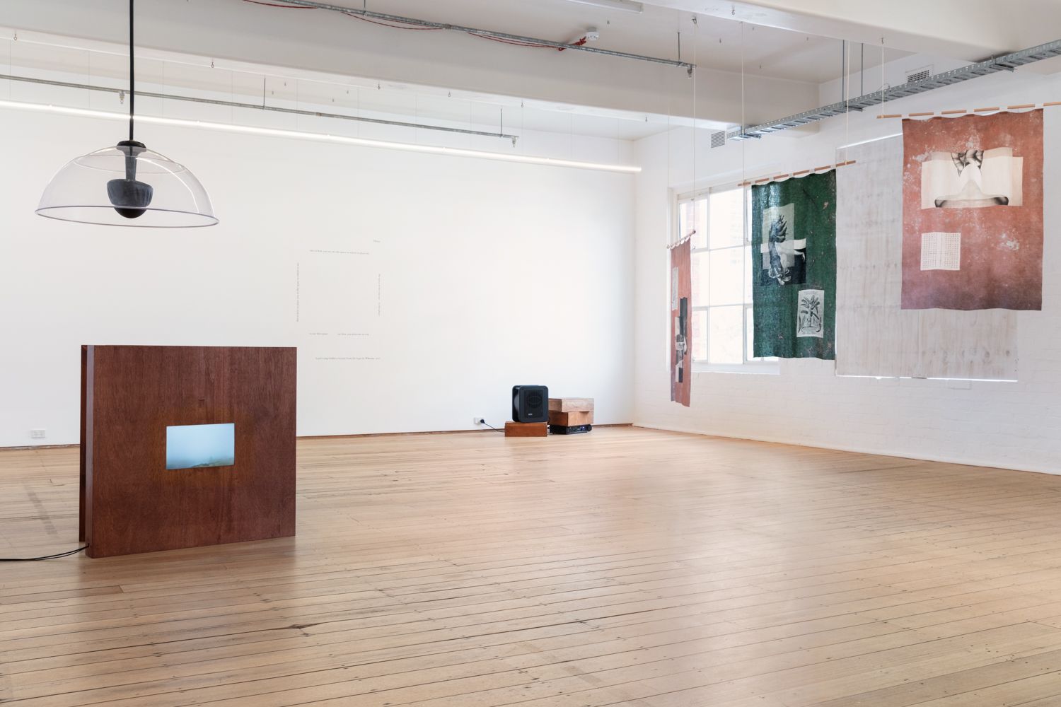 Install view of 'language to reach with' with Nithya Iyers textile works hanging to the right and Chi Trans work sitting on the floor to the left.