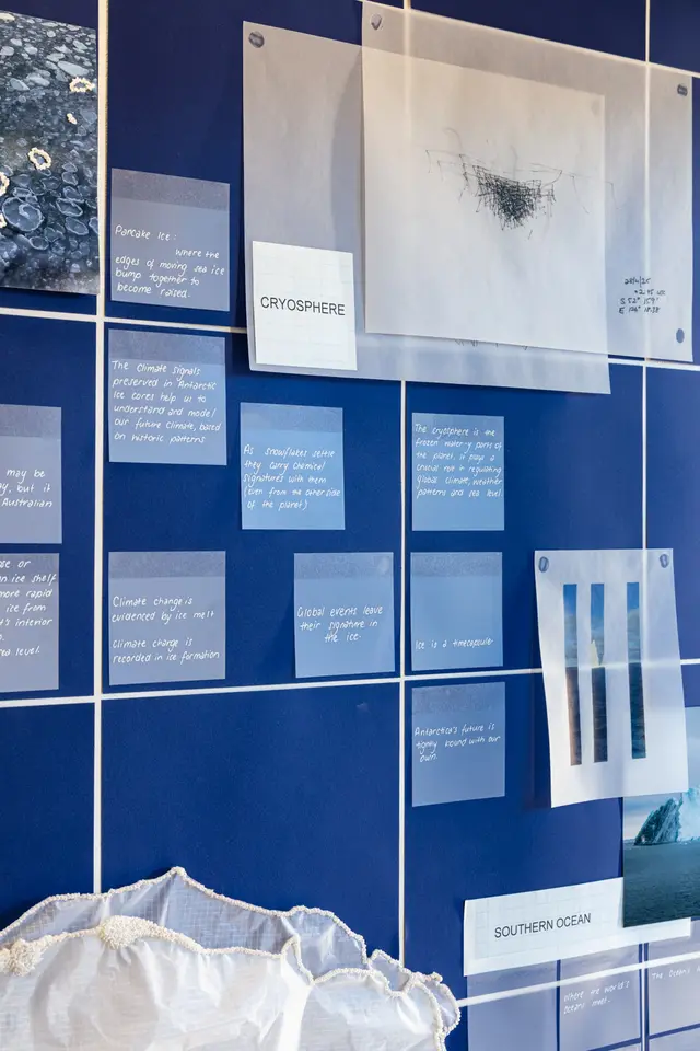 The background of deep blue squares and white intersections holds a number of square muted blue notes with white text. In the bottom left we see a glimpse of the sheer crinkled fabric.