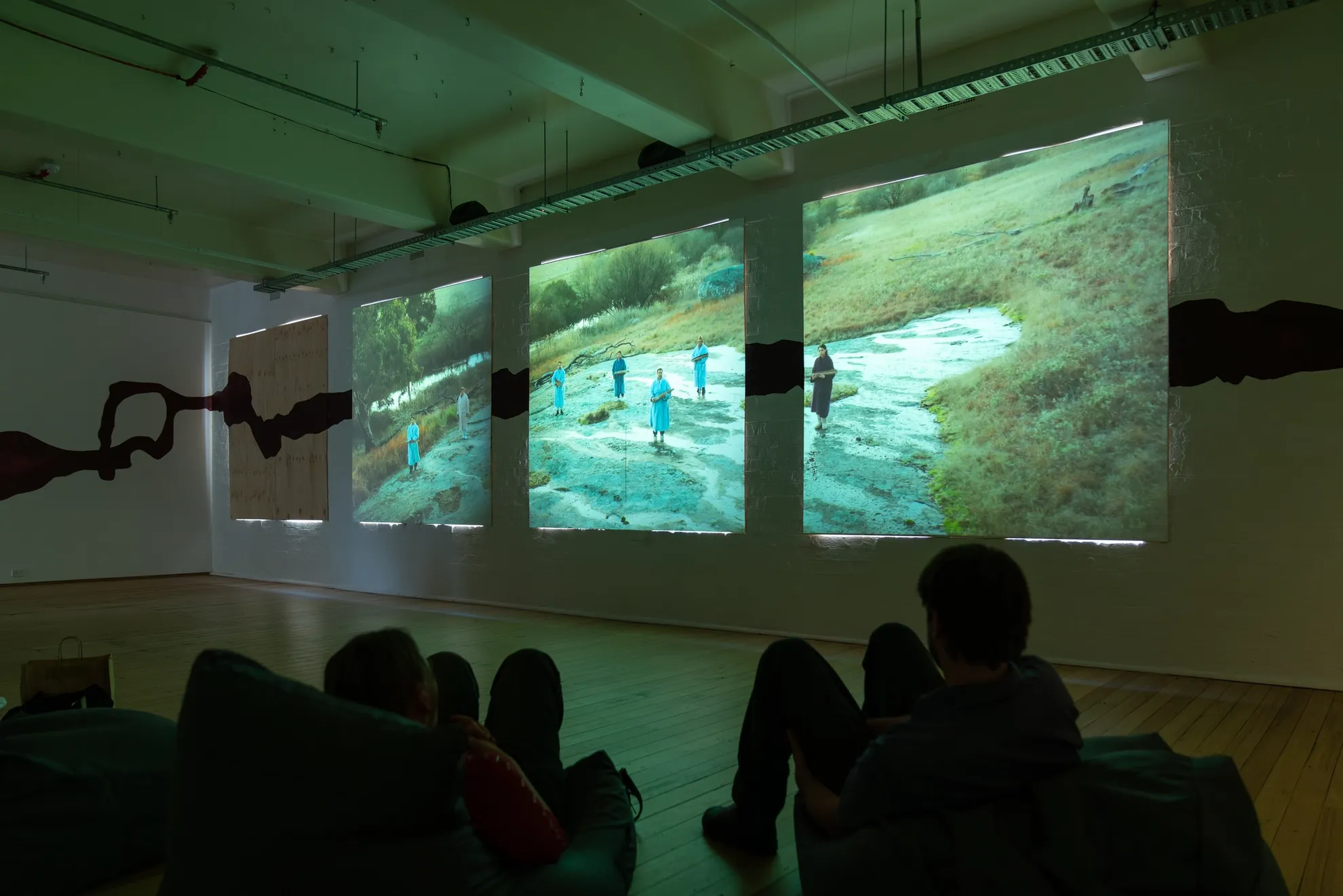 People watching videos displaying on three screens in the dark.