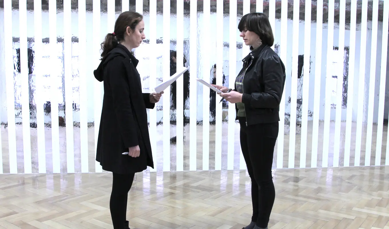 Two people standing facing each other holding sheets of paper and reading them.