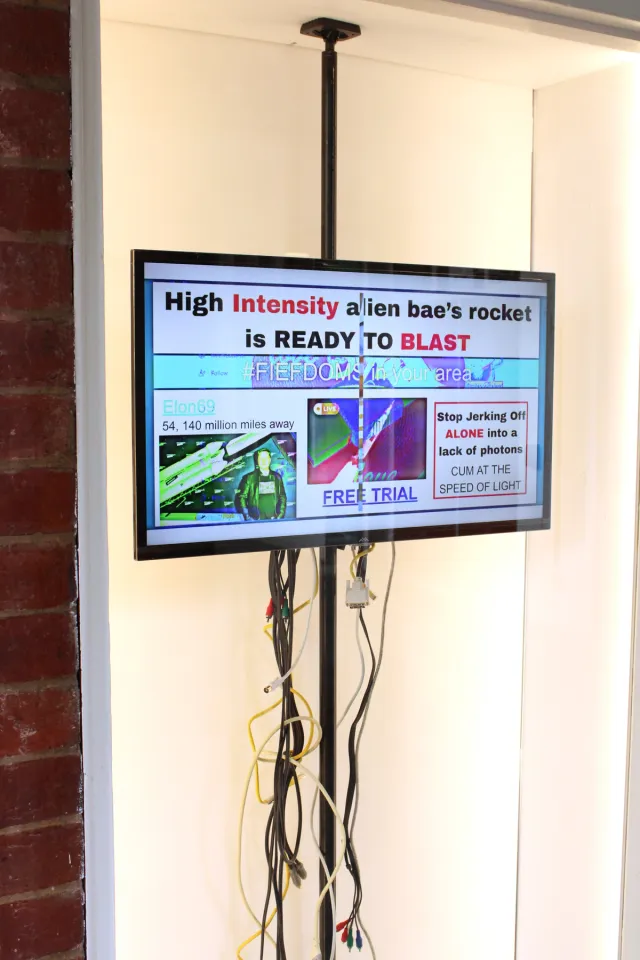 Behind a white framed window there is a tv displayed on a black pole. The screen shows a selection of various images and captions that appear to mimic a breaking news title.