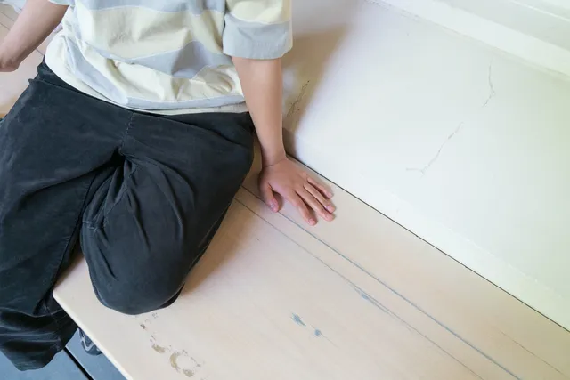 The lower part of a person wearing stripe shirt and black pants sitting on a bench..