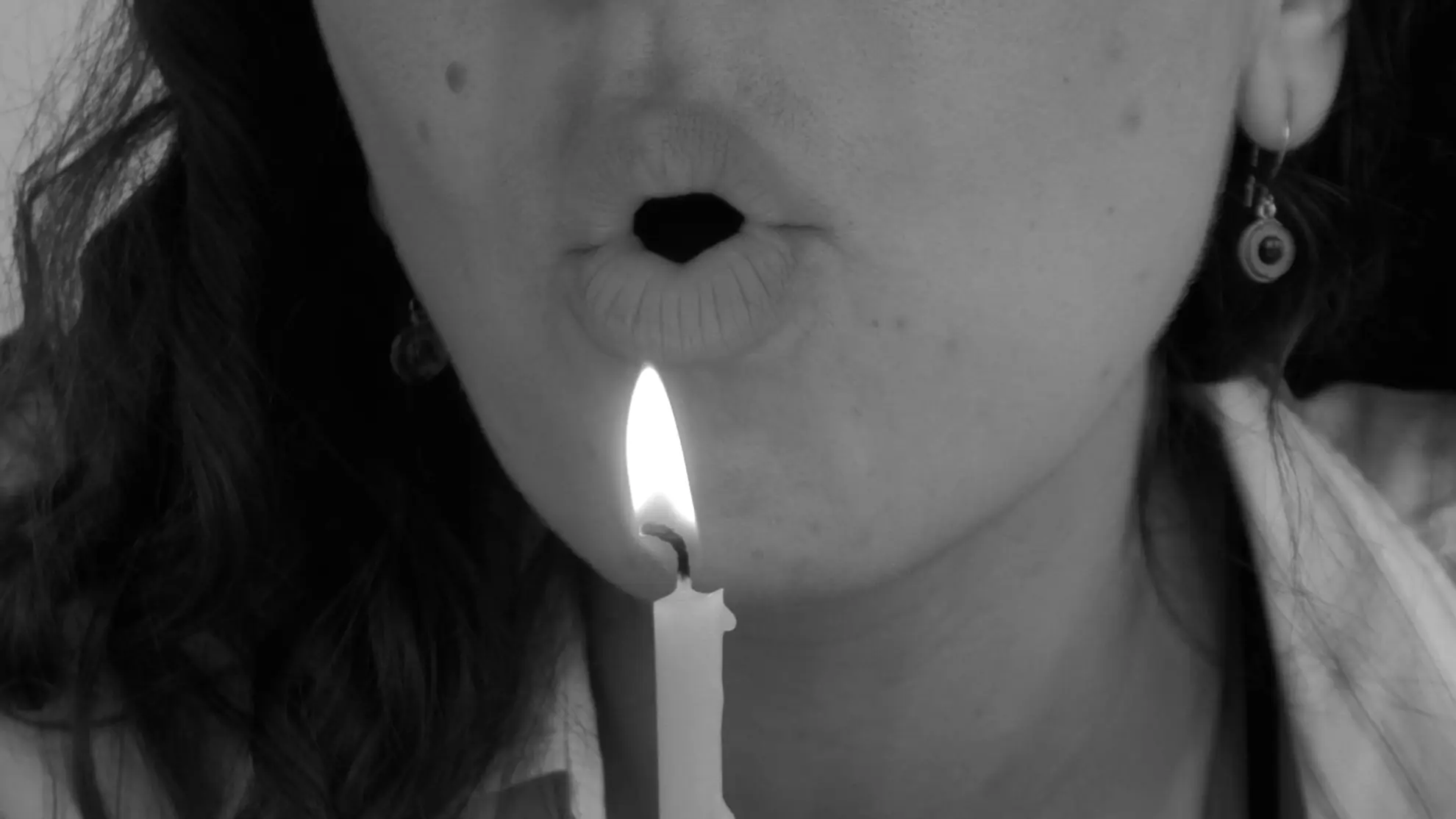 A close up film still of Tina with pursed lips blowing air on to a lit candle.