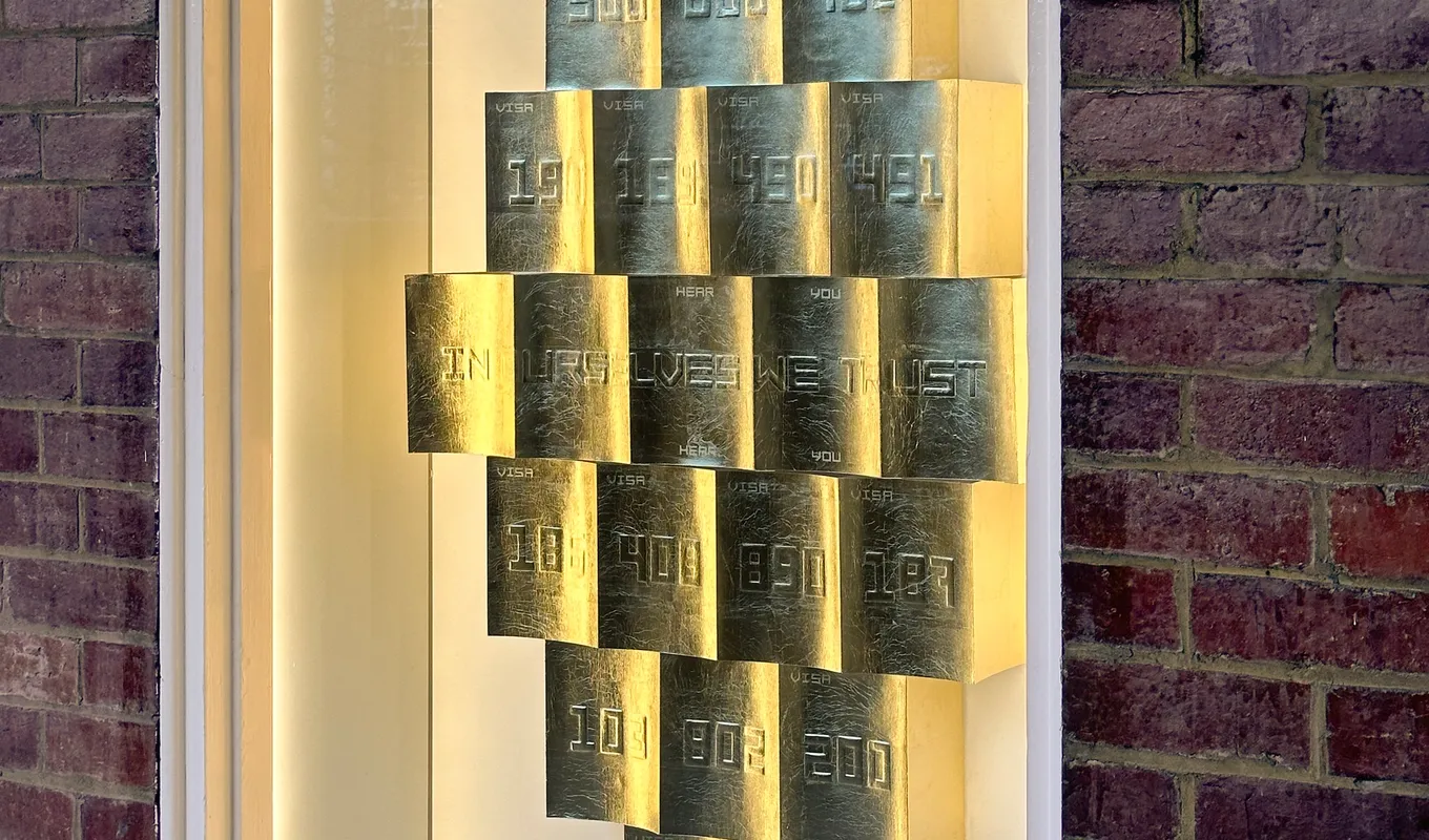 A close up installation view of the west space window. There are a collection of gold rectangular objects that are arranged in a diamond formation. These shapes are emobossed with 3 digit numbers representing the immigration visa codes in Australia