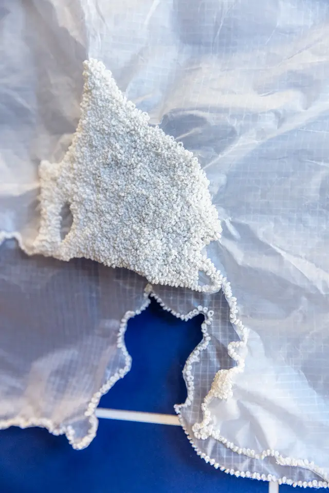 Detail shot of hundred of tiny beads embroidered onto sheer crinkled white fabric. The fabric lays on a deep blue background.