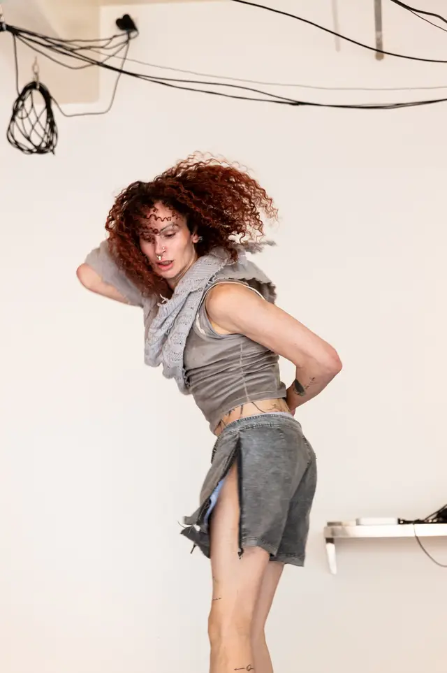 Andrea is standing in the middle, performing with one hand placed behind her head, the other on her back.